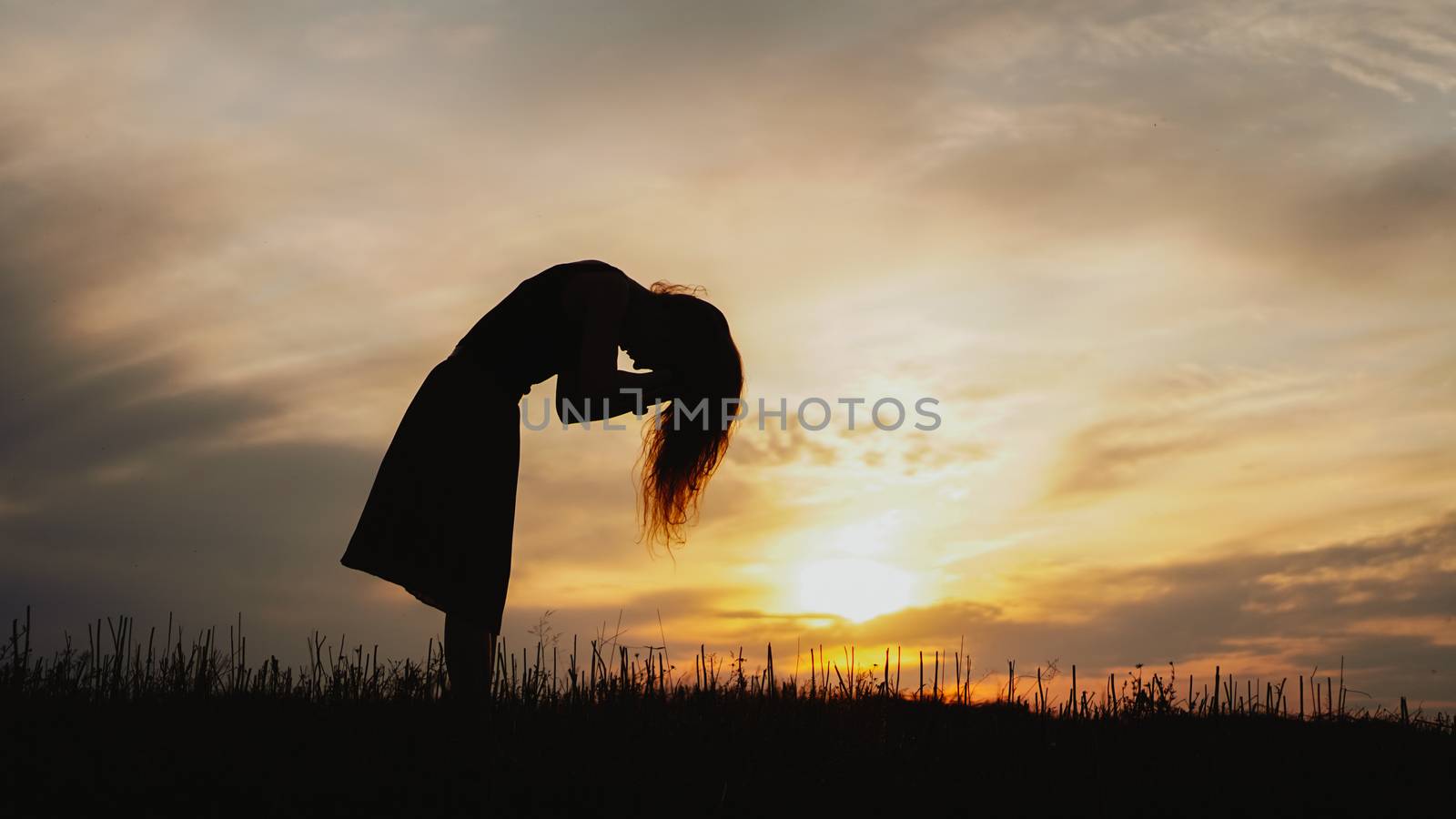 Silhouette of a young woman standing in dry grass field on bright sunset
