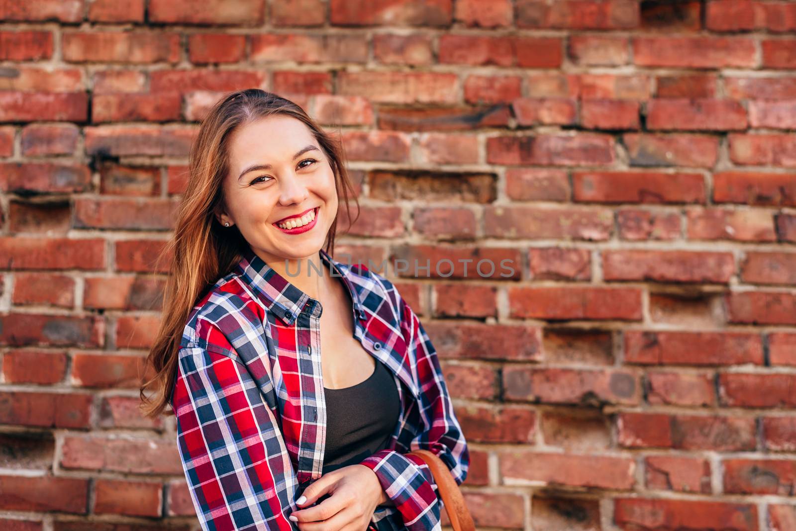 Portrait of young woman in checkered shirt standing against brick wall