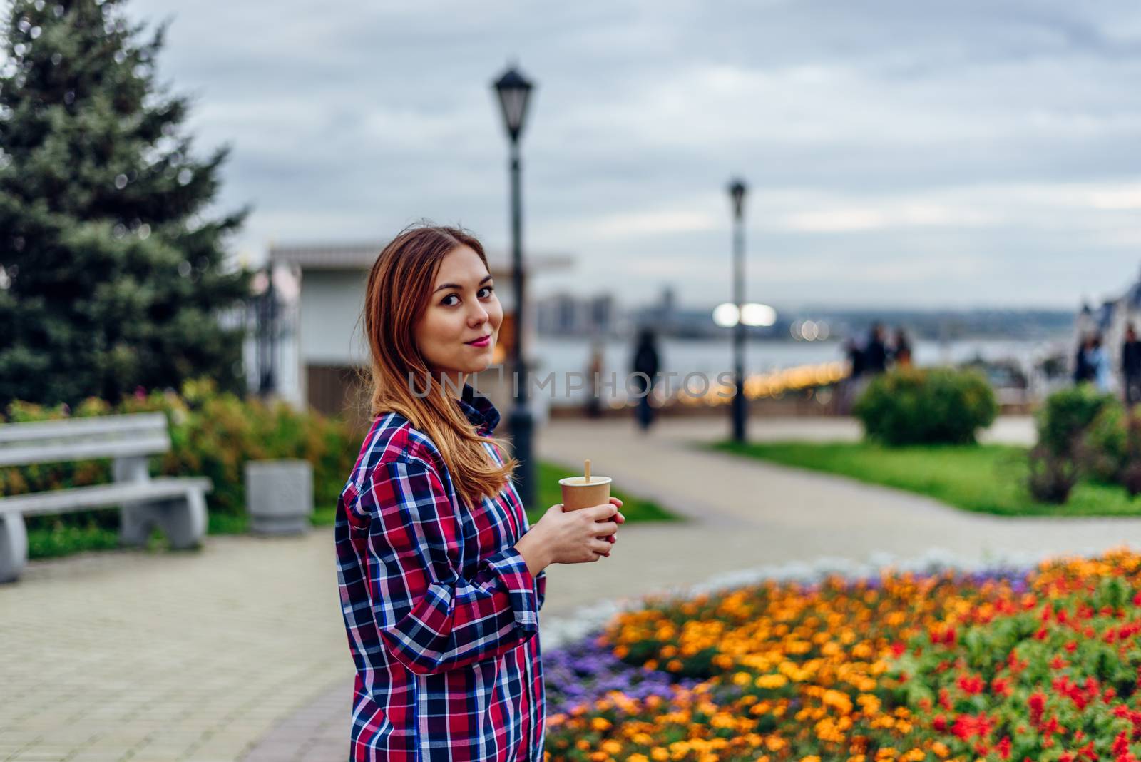 Beautiful young woman holding coffee cup and smiling in the park by Seva_blsv