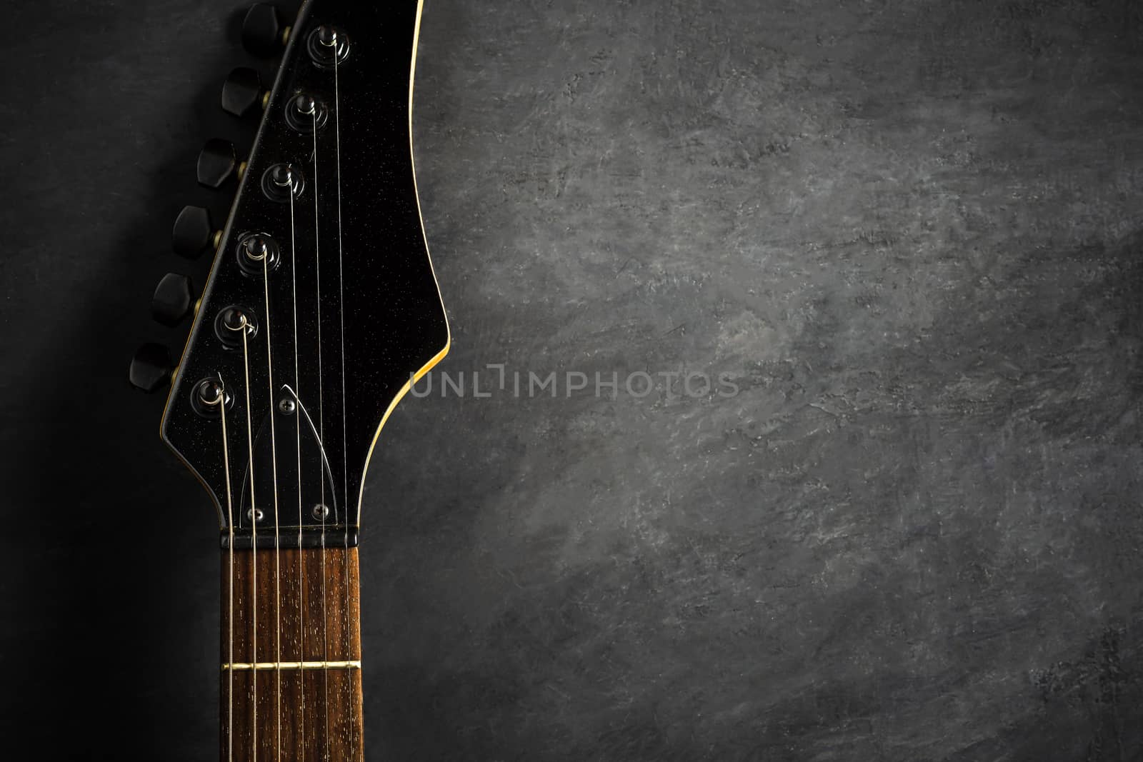 Headstock of black electric guitar on black cement floor. Top vi by SaitanSainam