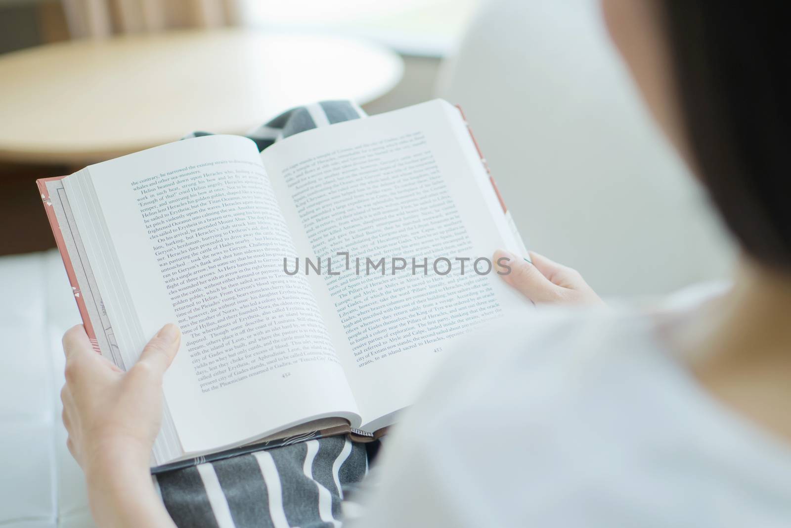 Woman with a book on her hands lying on a sofa in a living room by ekachailo