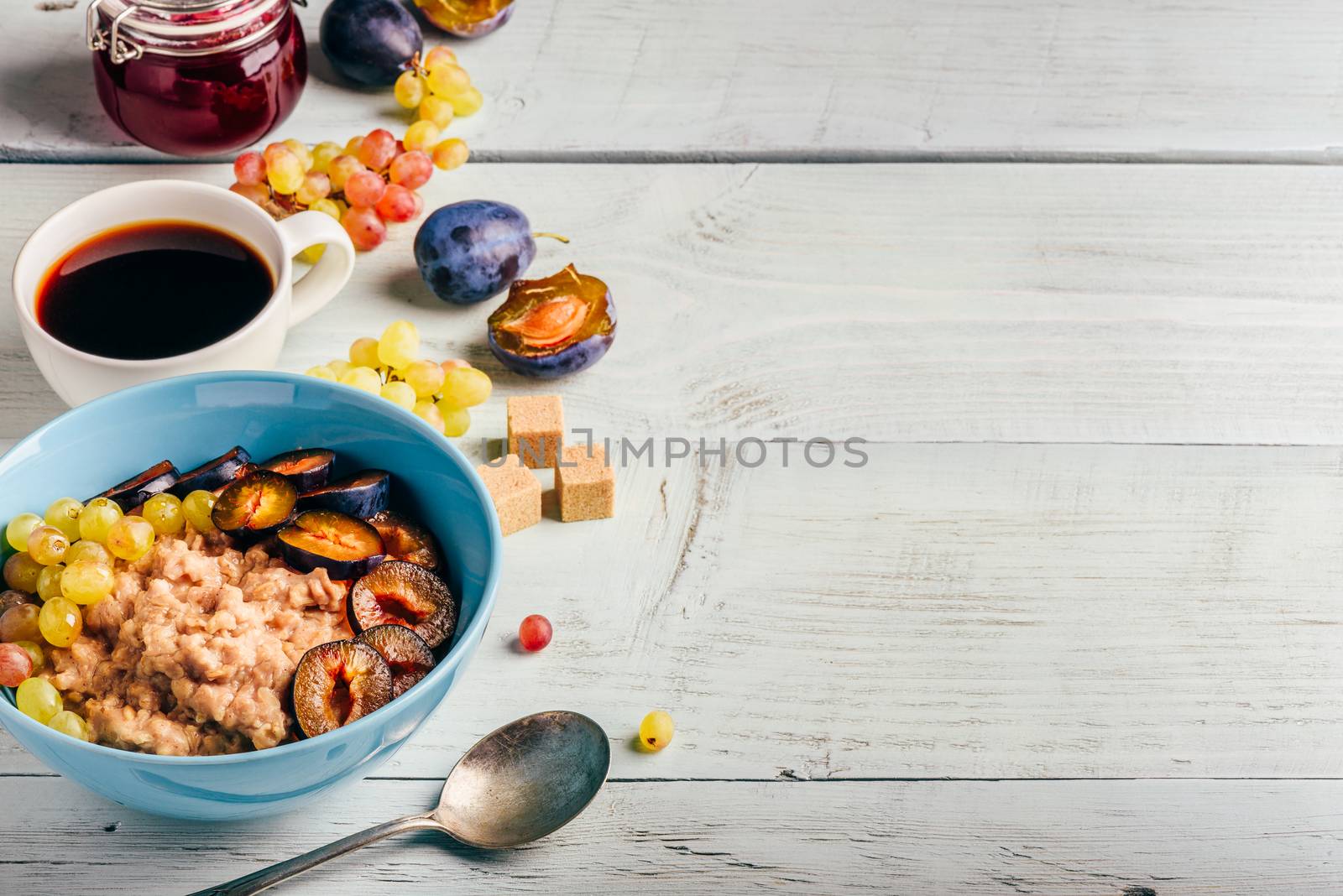 Healthy breakfast concept. Porridge with fresh plum, green grapes and cup of coffee. Ingredients over wooden background.