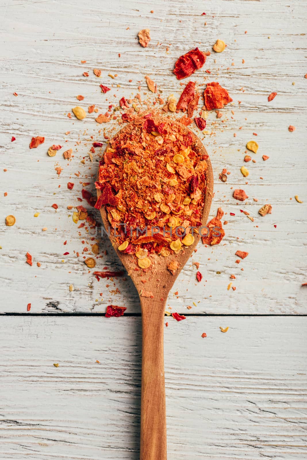 Spoonful of crushed red chili pepper over wooden background