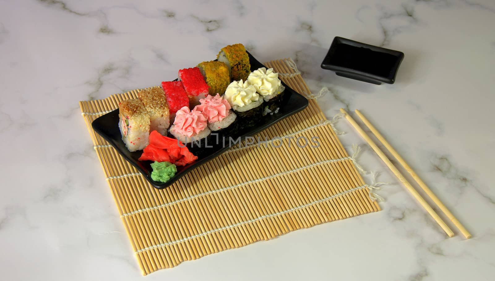 Sushi set with red ginger and wasabi on a bamboo napkin, bowl with soy sauce and chopsticks.