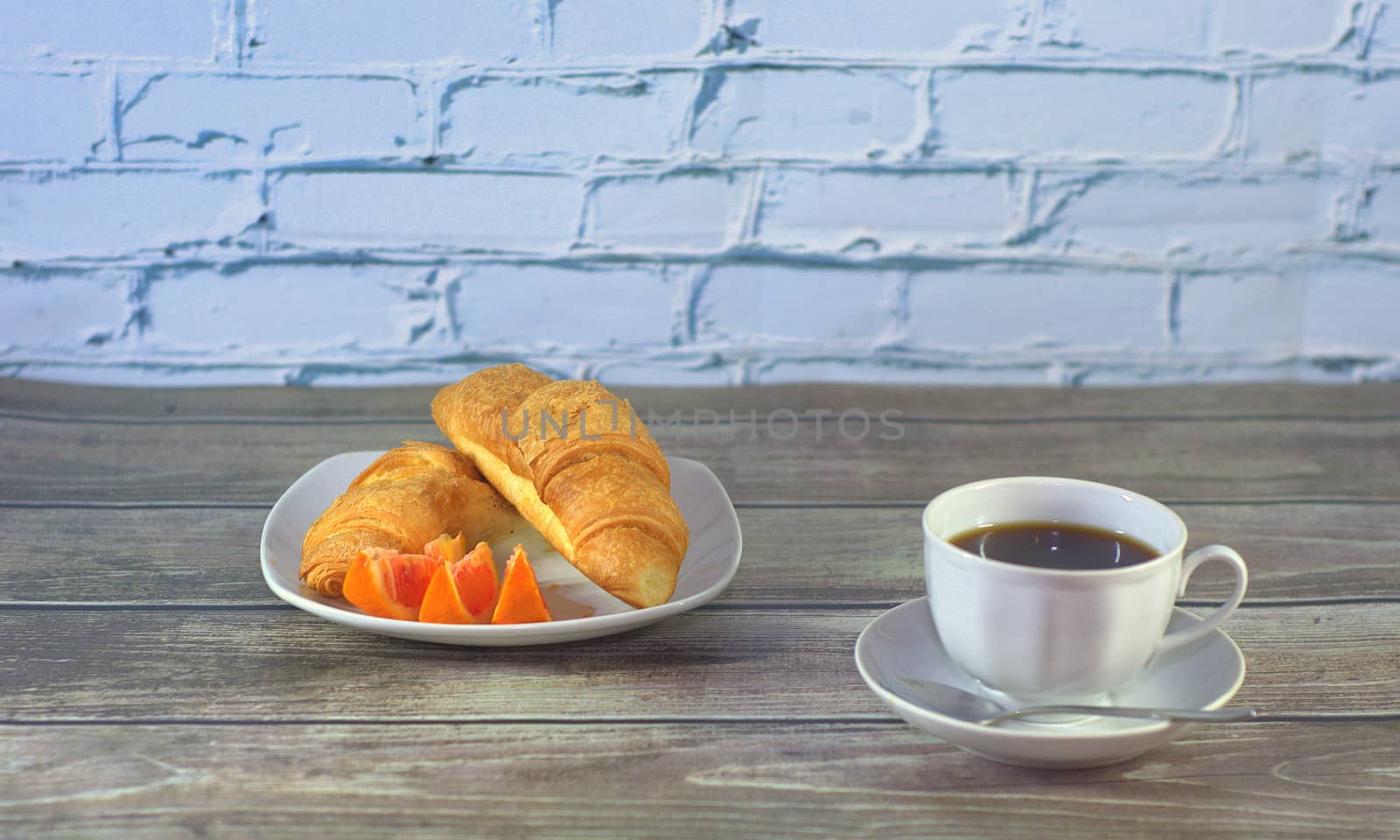 Traditional breakfast, a cup of black coffee, croissants, slices and orange on the table.