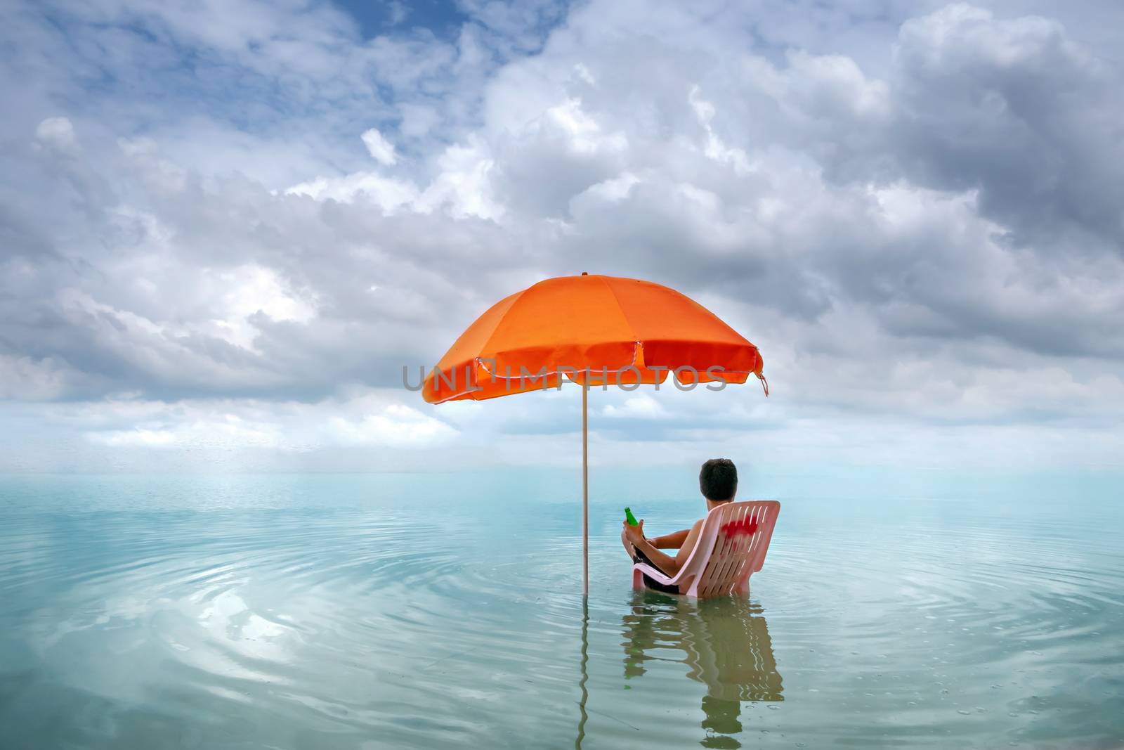 Happy man sitting on pink lounge chairs with  sun umbrella in a sea