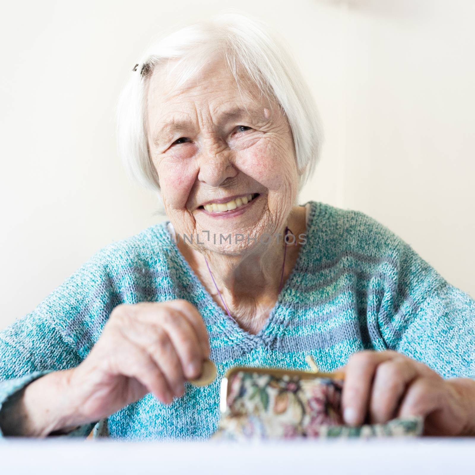 Cheerful elderly 96 years old woman sitting at table at home happy with her pension savings in her wallet after paying bills. by kasto