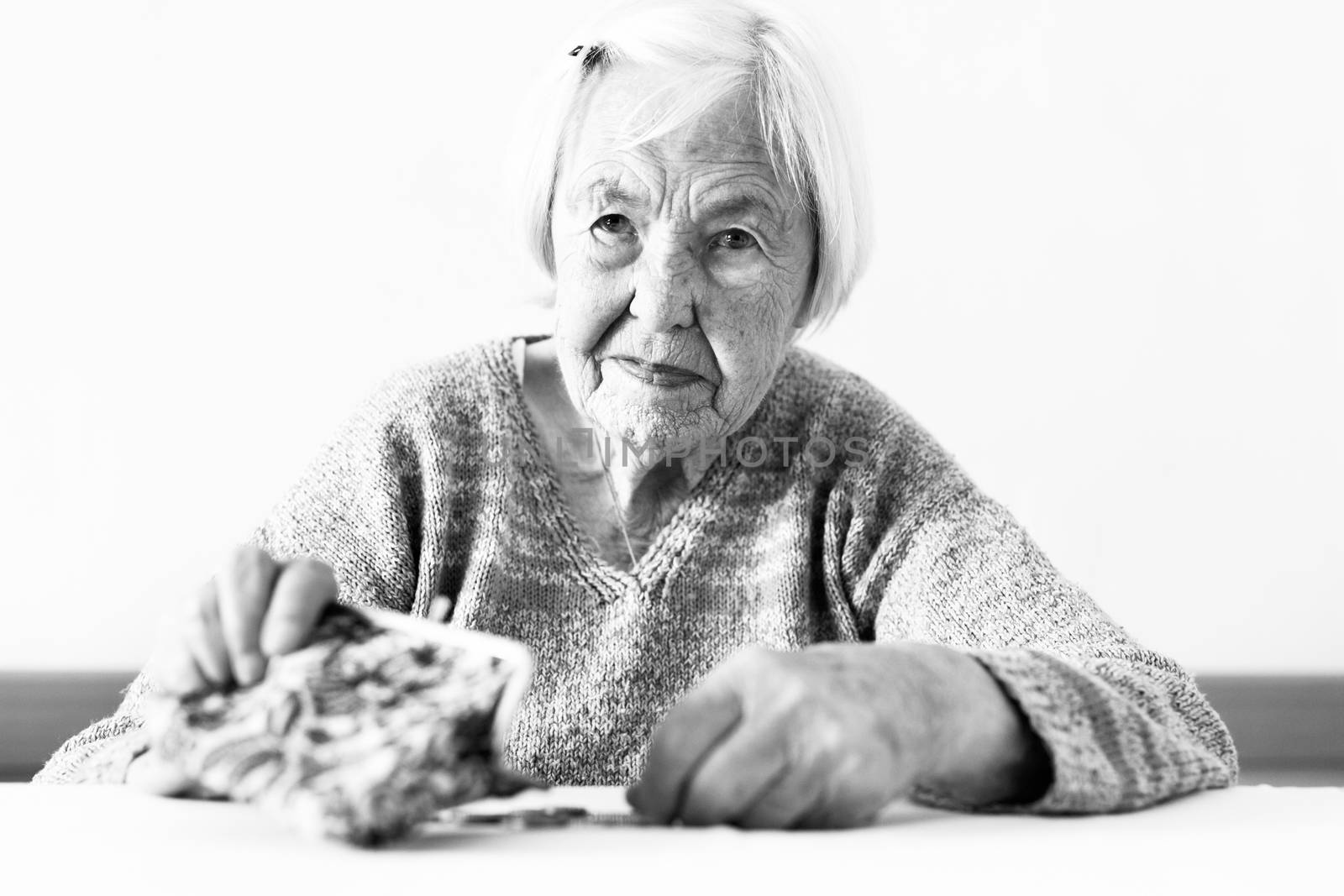 Concerned elderly 96 years old woman sitting at table at home and counting remaining coins from pension in her wallet after paying bills. Unsustainability of social transfers and pension system.