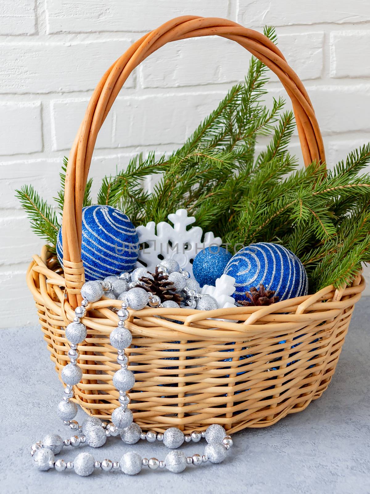 Christmas composition - wicker basket with decorations and fir branches on a light background.