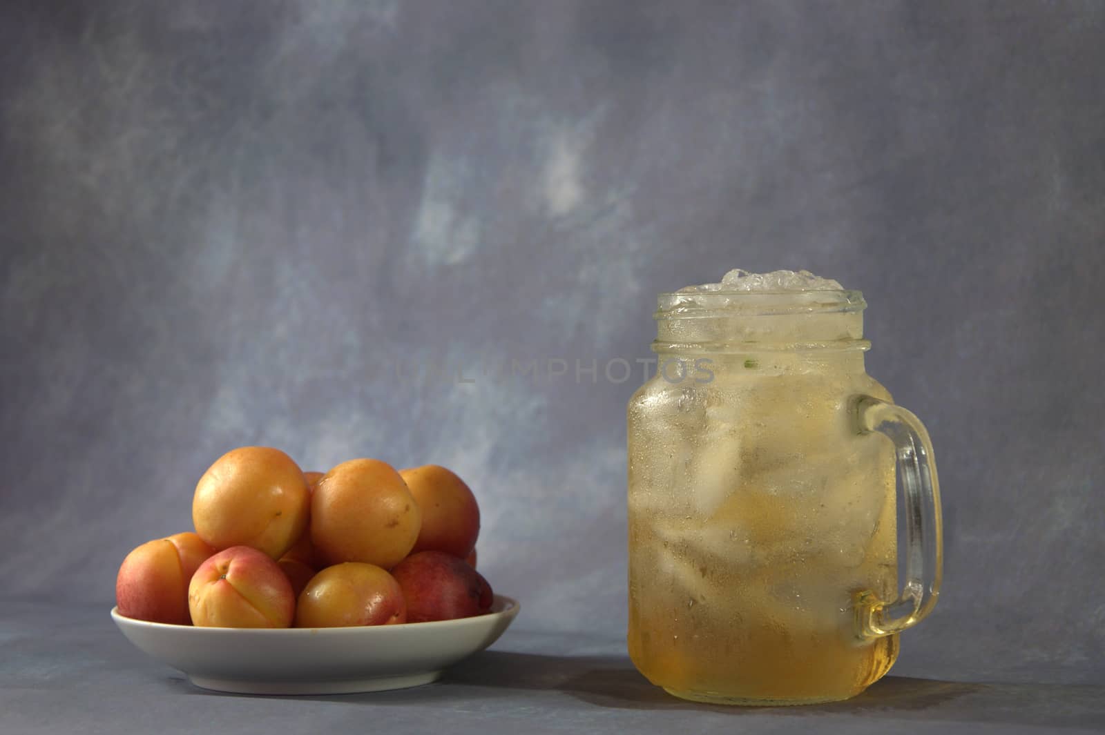 A few fresh apricots on a plate and a cup of apricot juice with ice.