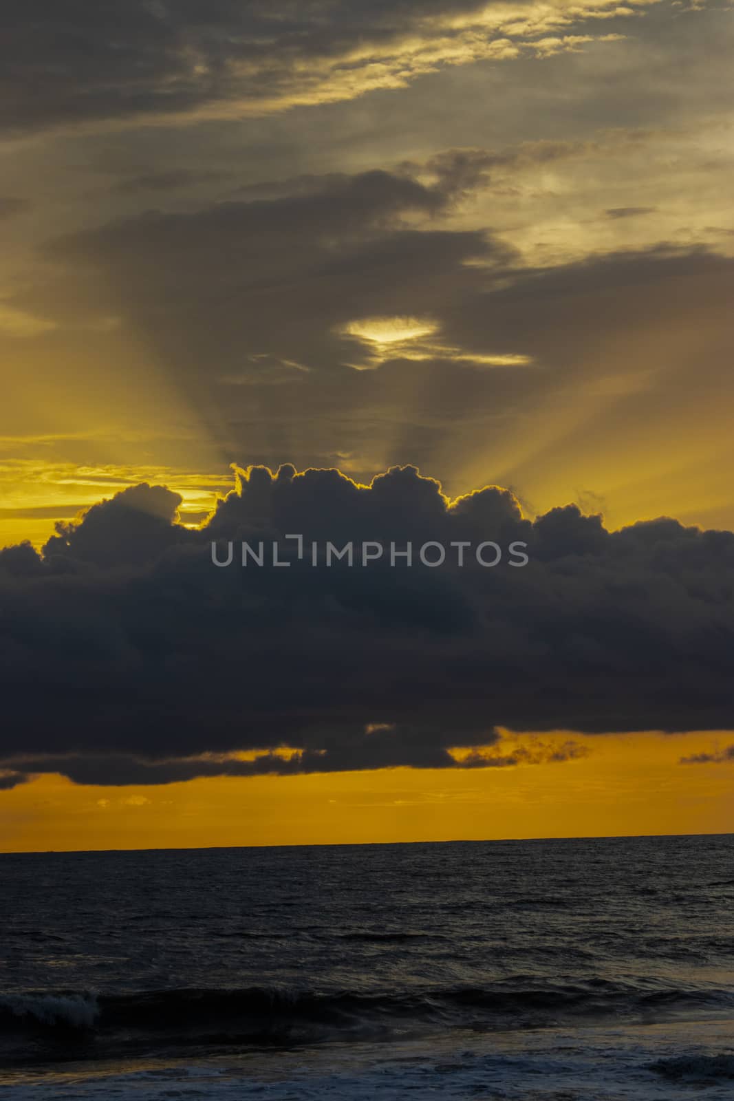 Orange sky with rays of sun coming from the backside of the cloud above the sea