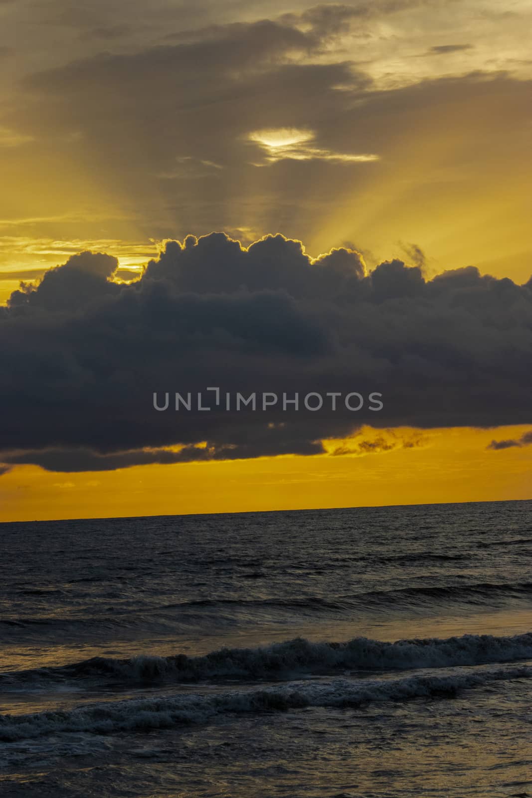 Orange sky with rays of sun coming from the backside of the cloud above the sea