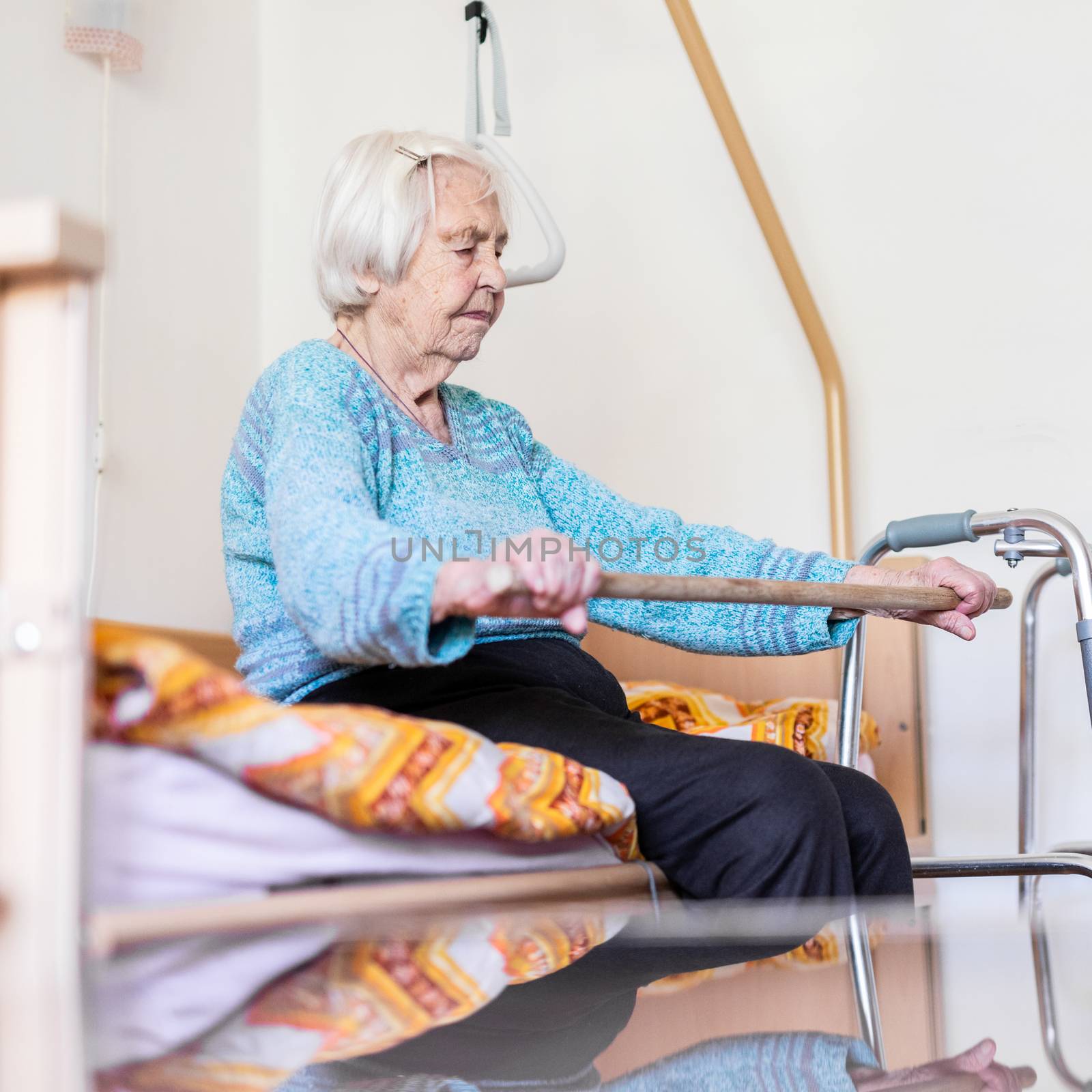 Elderly 96 years old woman exercising with a stick sitting on her bad. Geriatric health care home assisted support for older people concept. Care for the elderly.