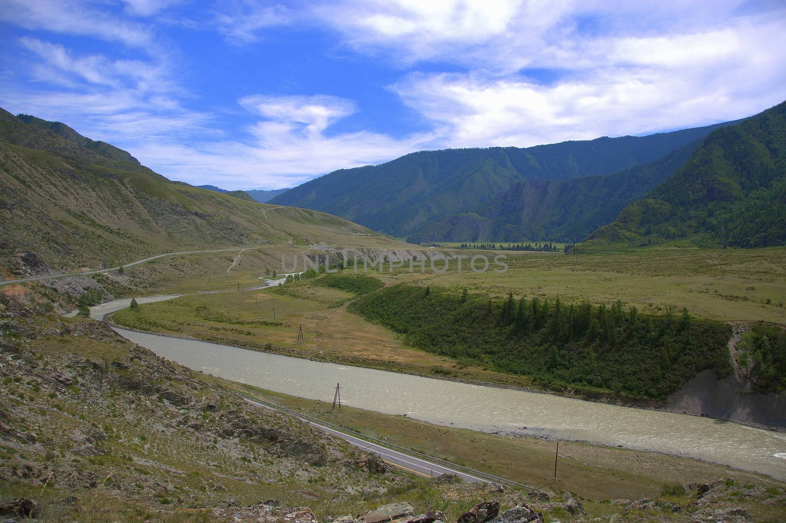 A picturesque valley in the mountains, an asphalt road and a stormy river crossing the countryside. Chuya River, Altai, Siberia, Russia.