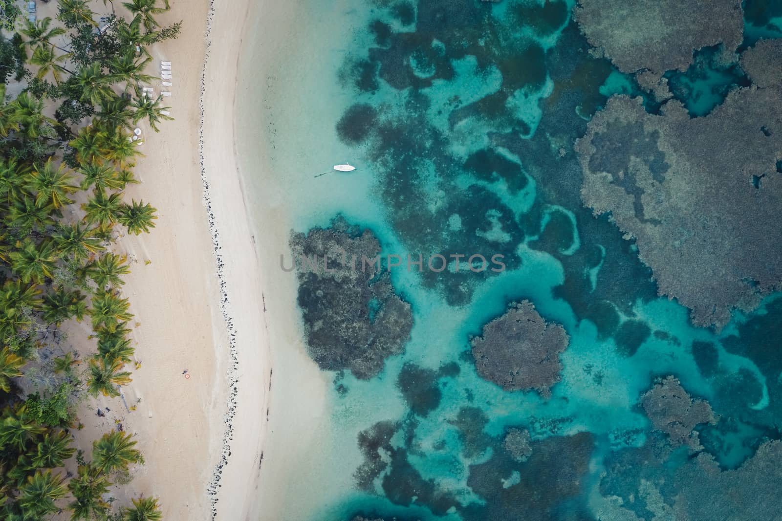 Drone shot of tropical beach with white boat anchored.Samana peninsula,Grand Bahia Principe El Portillo beach,Dominican Republic.