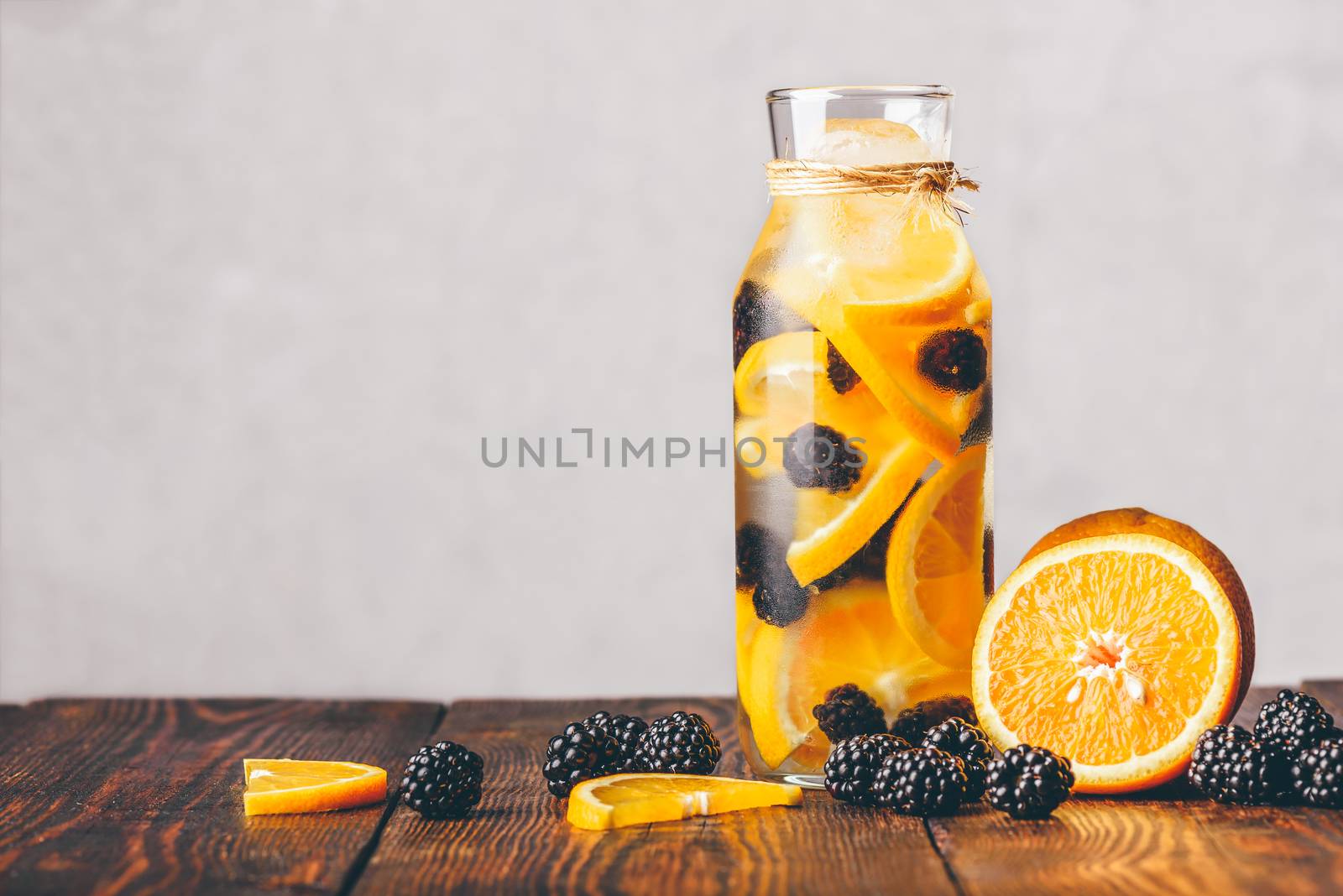 Bottle of Water Infused with Sliced Raw Orange and Fresh Blackberry. Ingredients on Wooden Table.