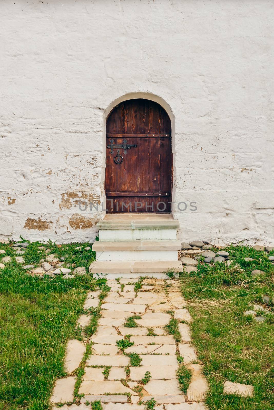Old, Brown, Wooden Door on White Brick Wall with Stone Path and Grass
