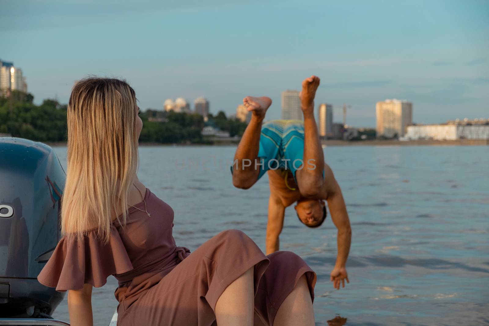 The guy jumps into the water from the boat. A beautiful girl is watching him