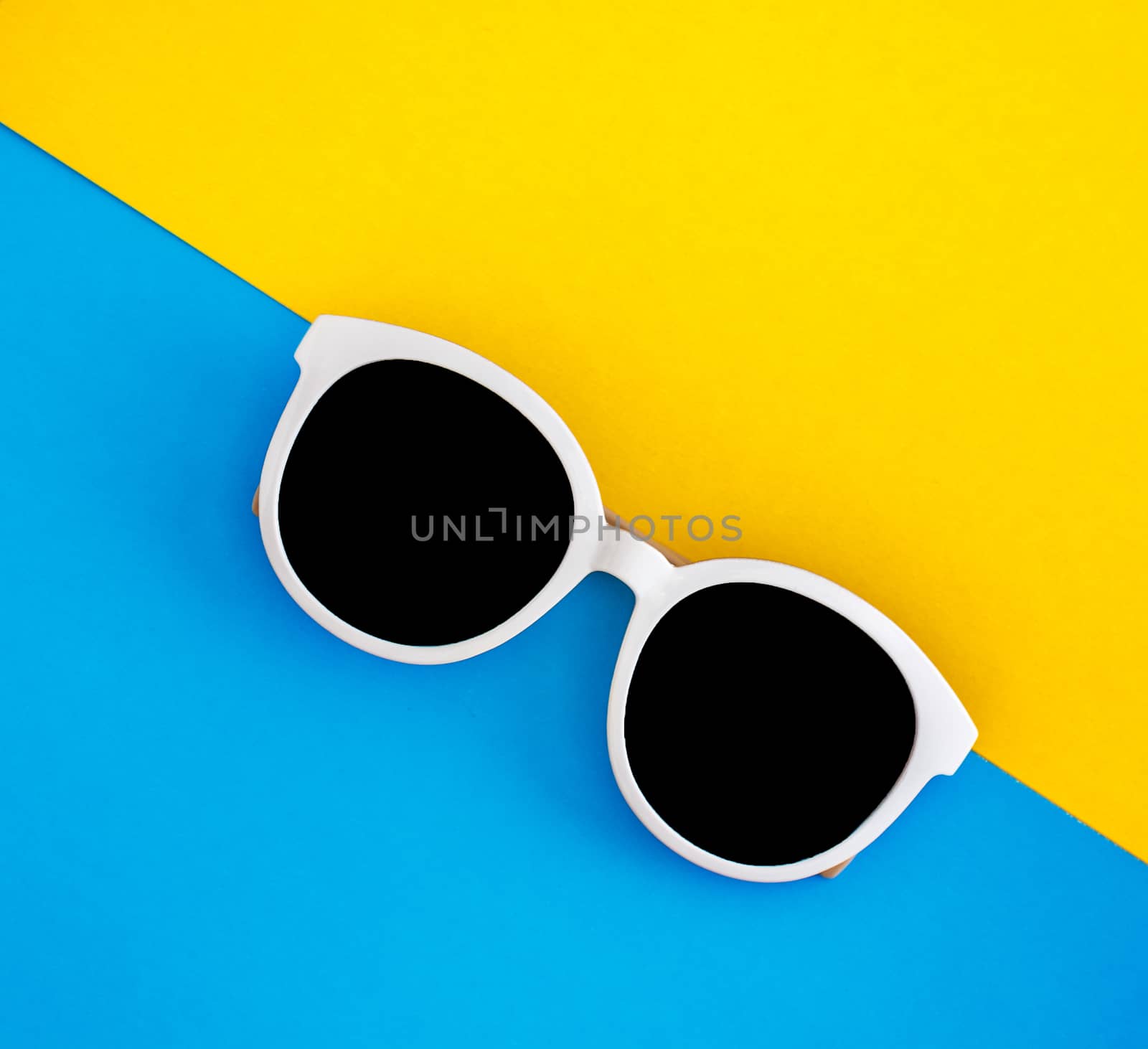 Sunny stylish white sunglasses on a bright blue-cyan and yellow-orange background, top view, isolated. Copy space. Flat lay.