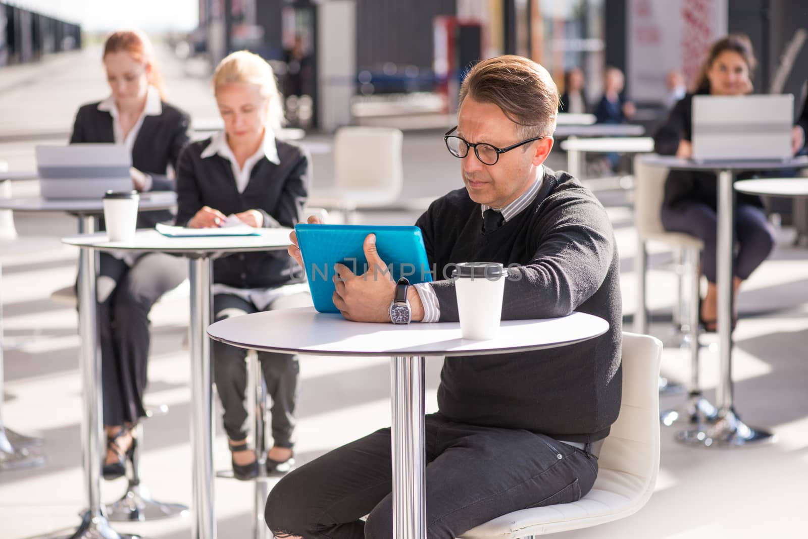 Many business people sitting in cafe , focus on man with tablet pc