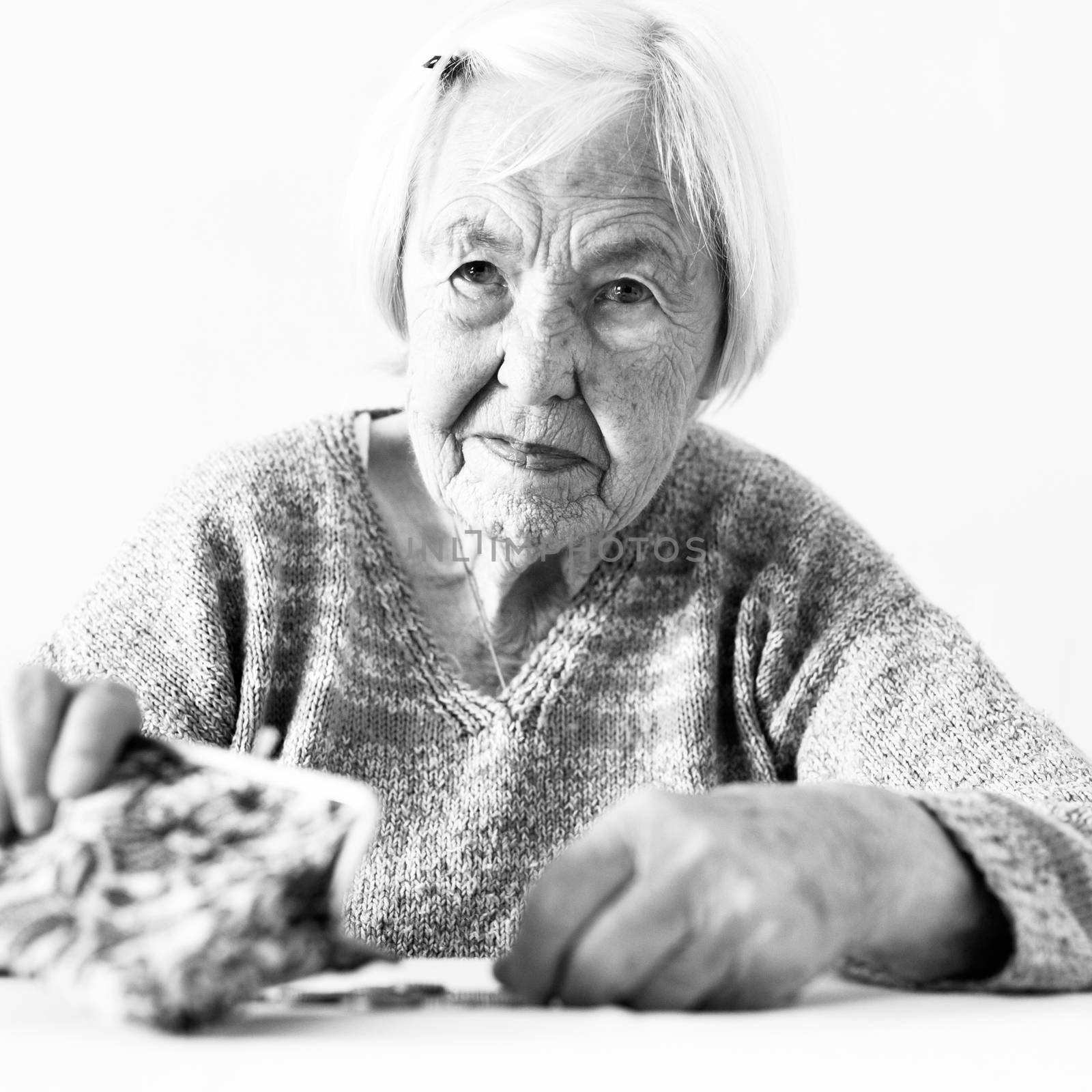 Concerned elderly woman sitting at the table counting money in her wallet. Black and white photo. by kasto