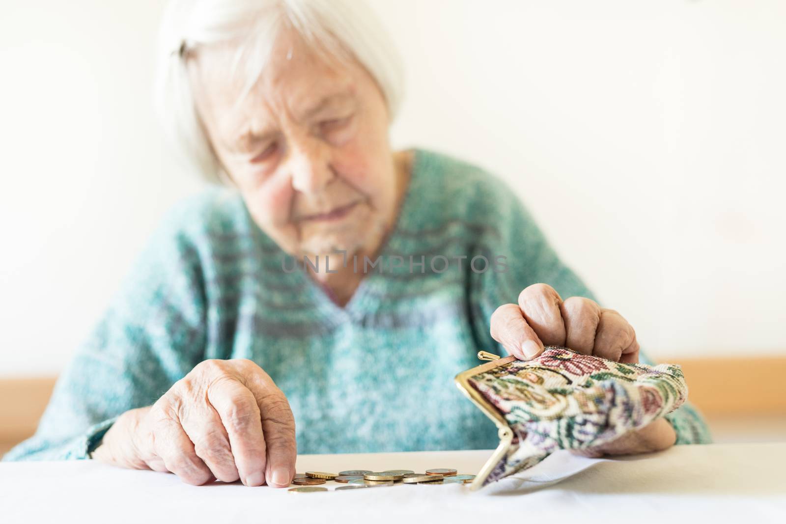 Concerned elderly 96 years old woman sitting at table at home and counting remaining coins from pension in her wallet after paying bills. Unsustainability of social transfers and pension system.