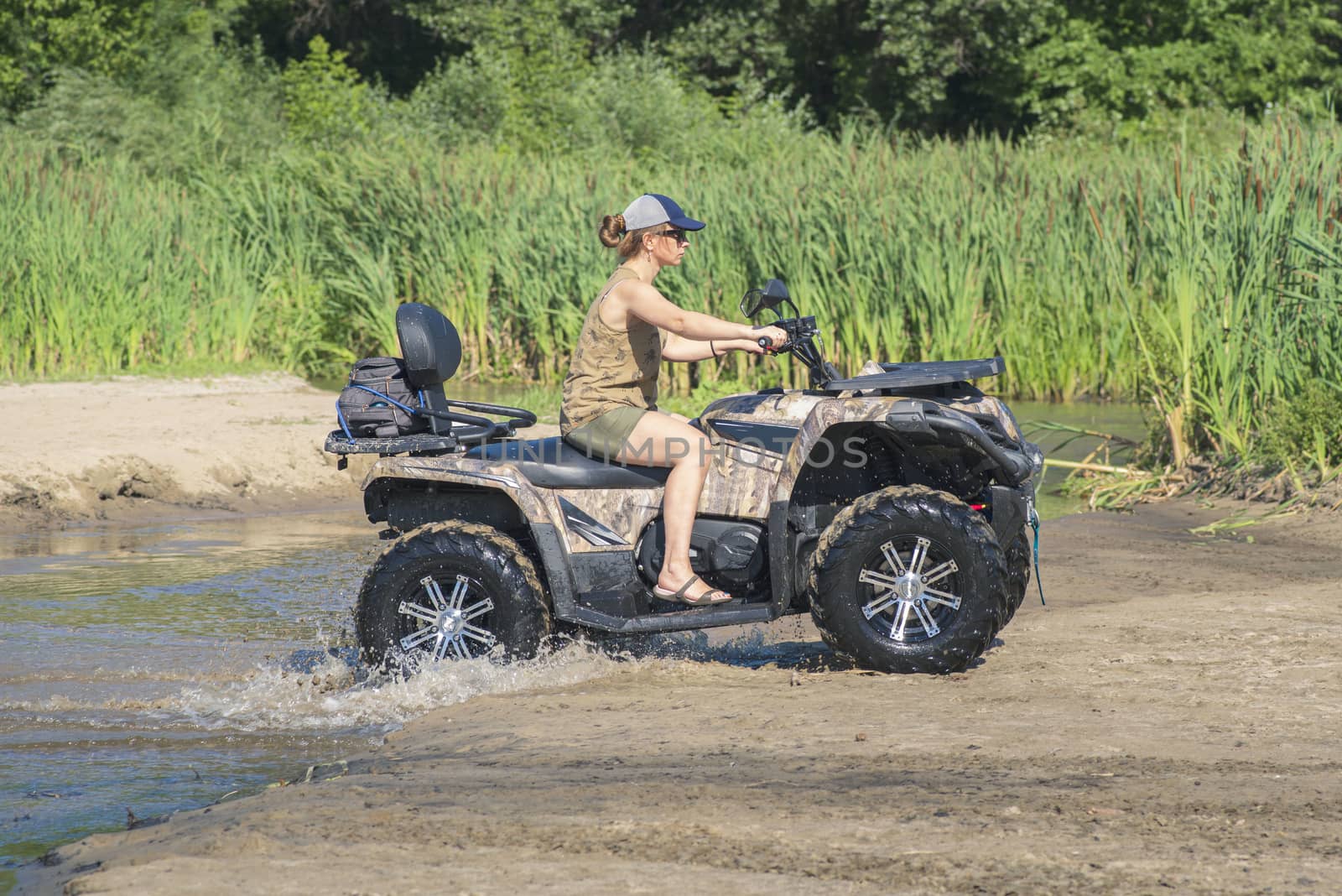 A girl on a Quad bike riding on the beach. A happy woman riding a quad bike on the river.