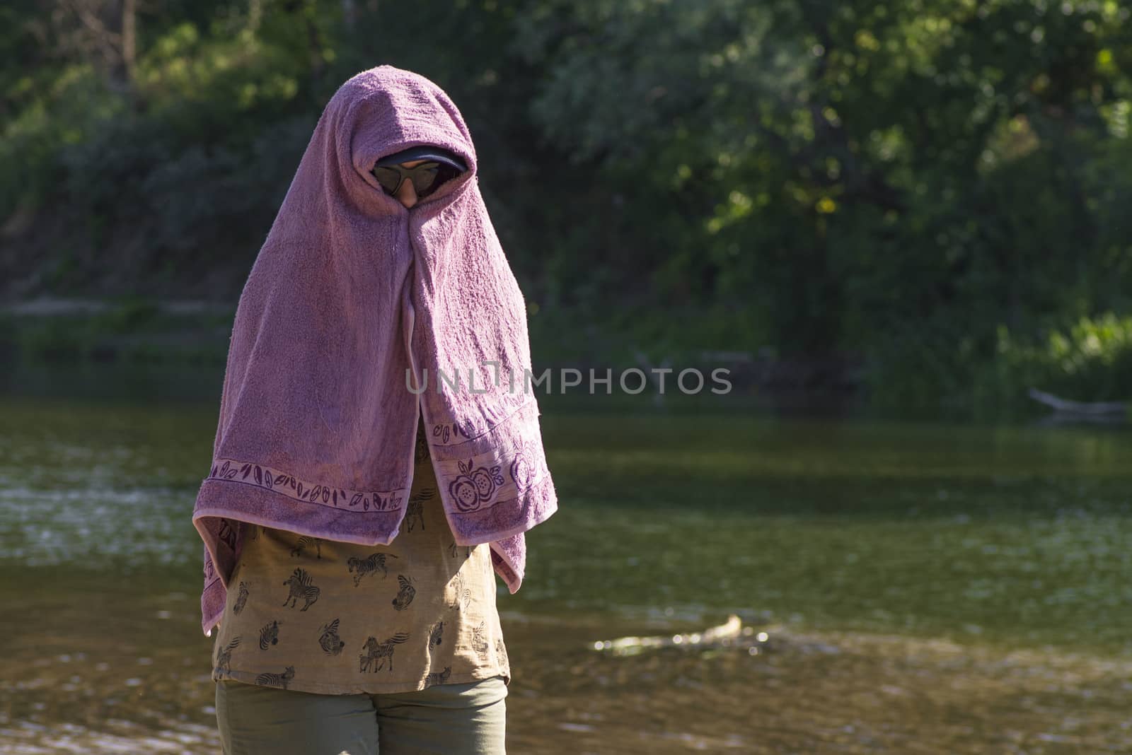 The girl hid her face from the bright sun under a towel.The girl is sitting on the beach with a towel on her head.