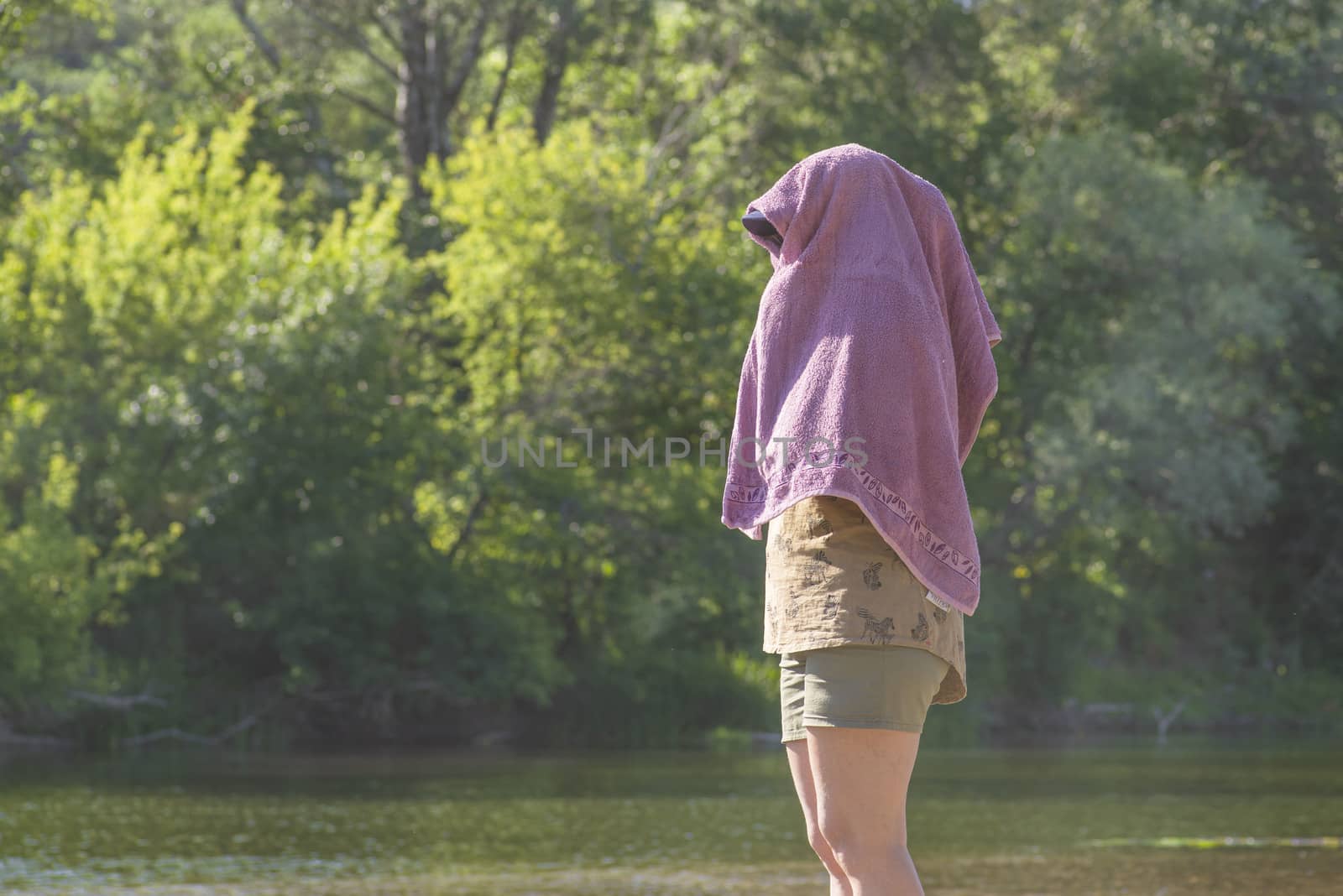 The girl hid her face from the bright sun under a towel.The girl is sitting on the beach with a towel on her head.