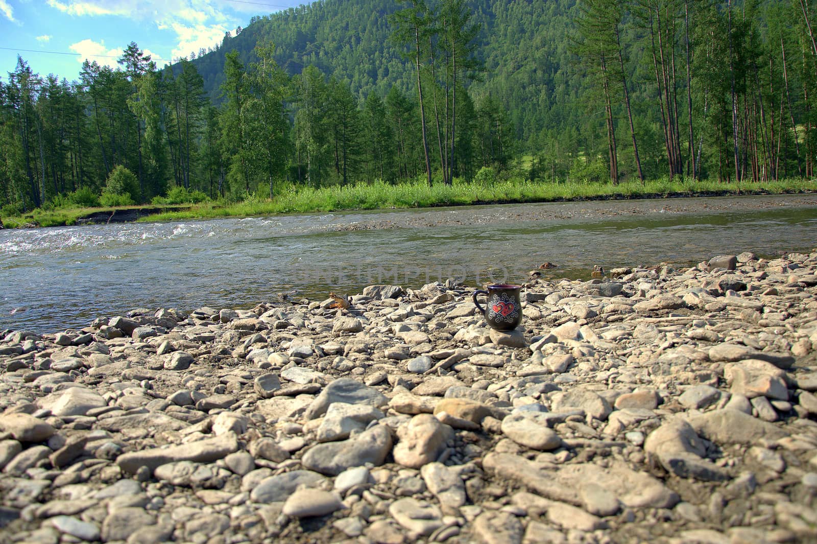 Morning coffee, a cup with a drink stands on a stone on the bank of a stormy mountain river. Ongudai, Altai, Siberia, Russia.