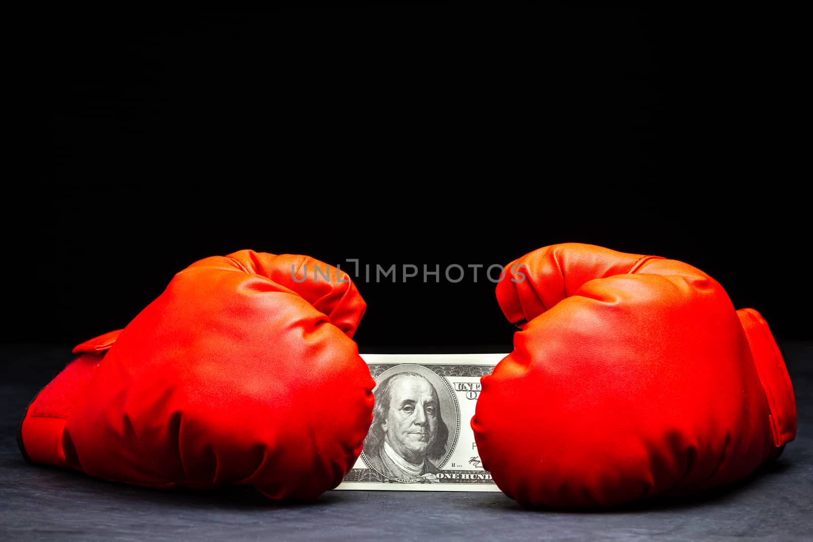Red boxing gloves holding the dollar banknote on cement floor in darkness. Concept of fighting for money or business battles.