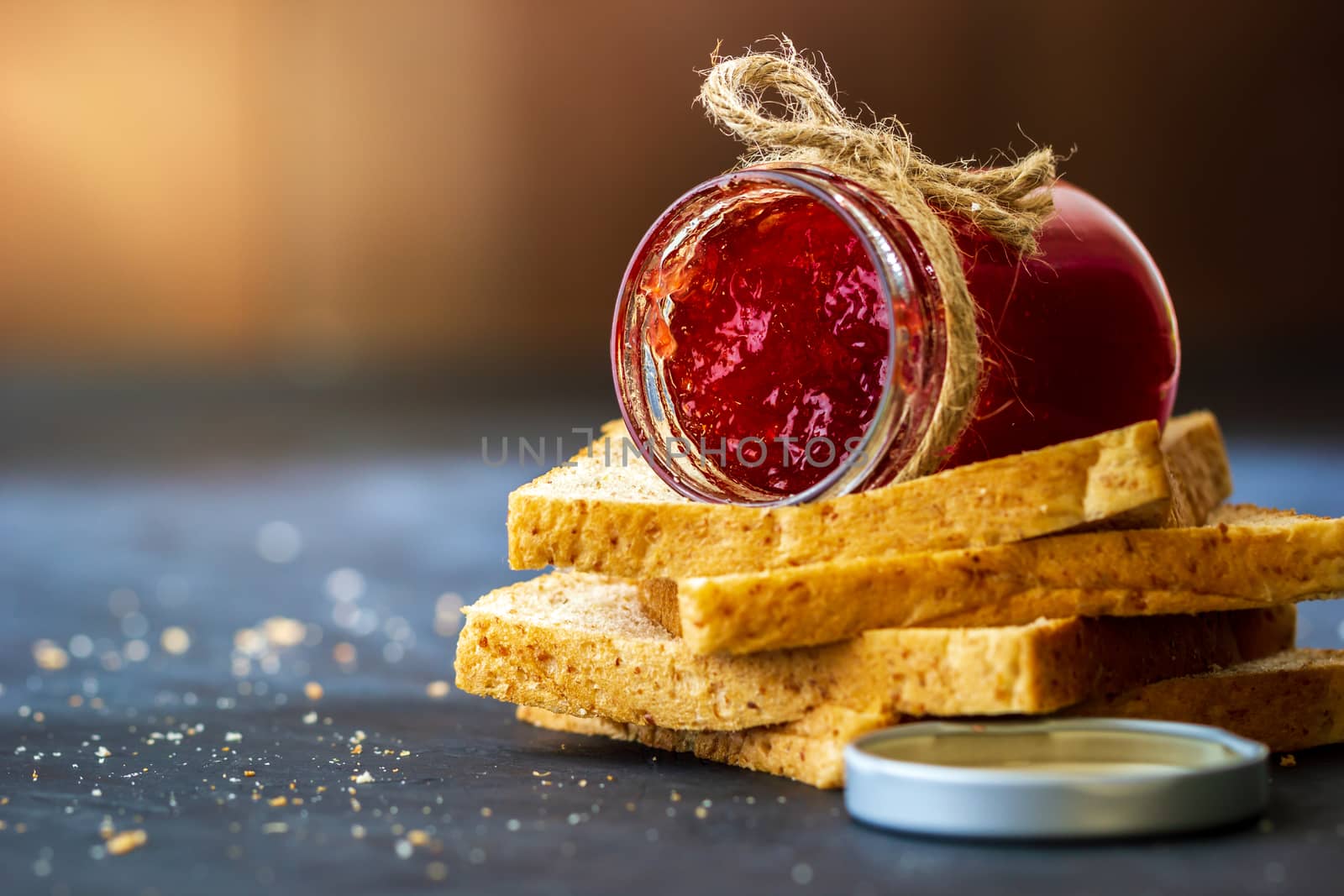 Strawberry jam bottle and whole wheat bread are stacked on a bla by SaitanSainam