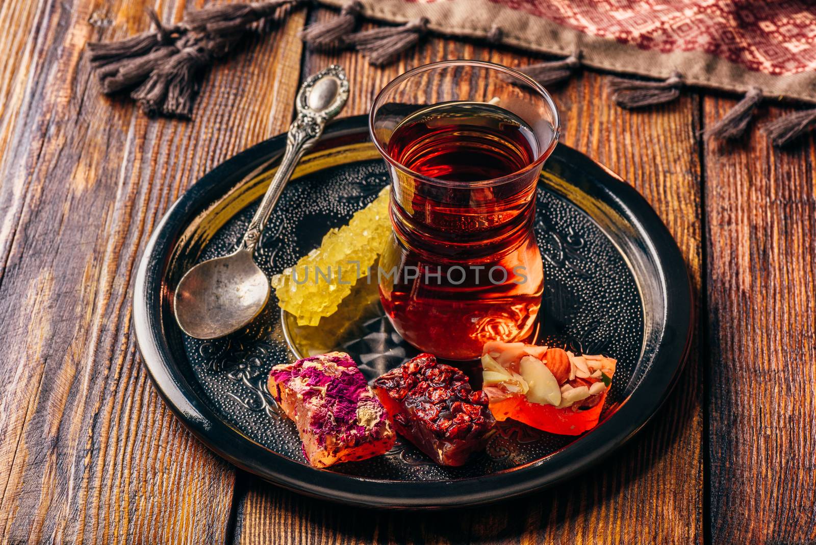 Tea in armudu glass with oriental delight rahat lokum on metal tray over wooden surface and tablecloth