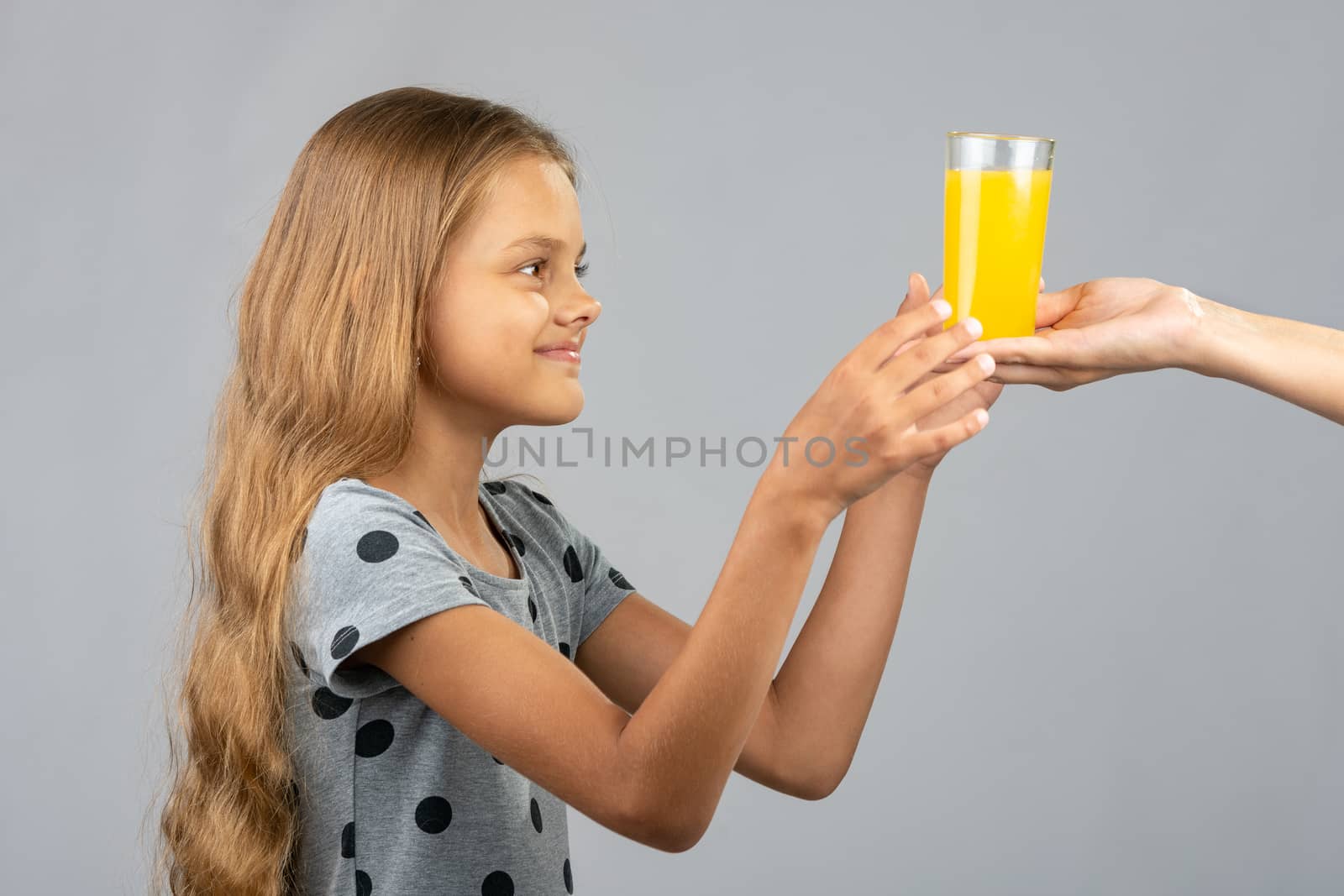 A girl with two hands takes a glass of juice from the hand of another person