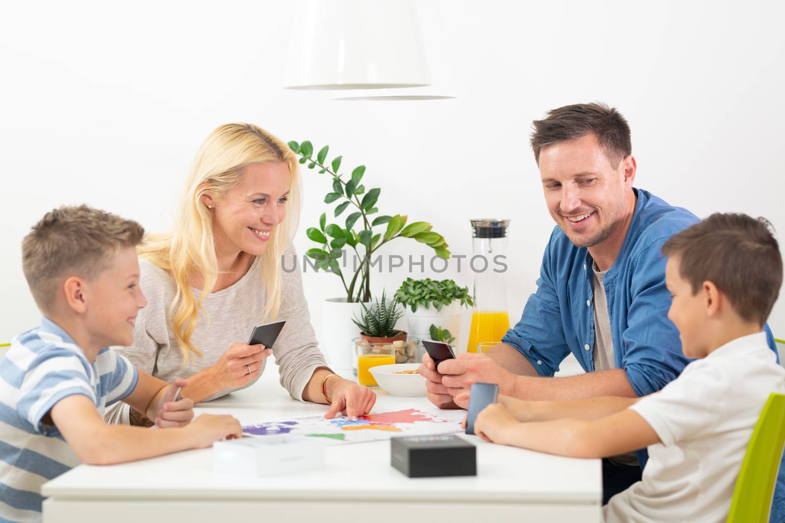 Happy young family playing card game at dining table at bright modern home. Spending quality leisure time with children and family concept. Cards are generic and debranded.