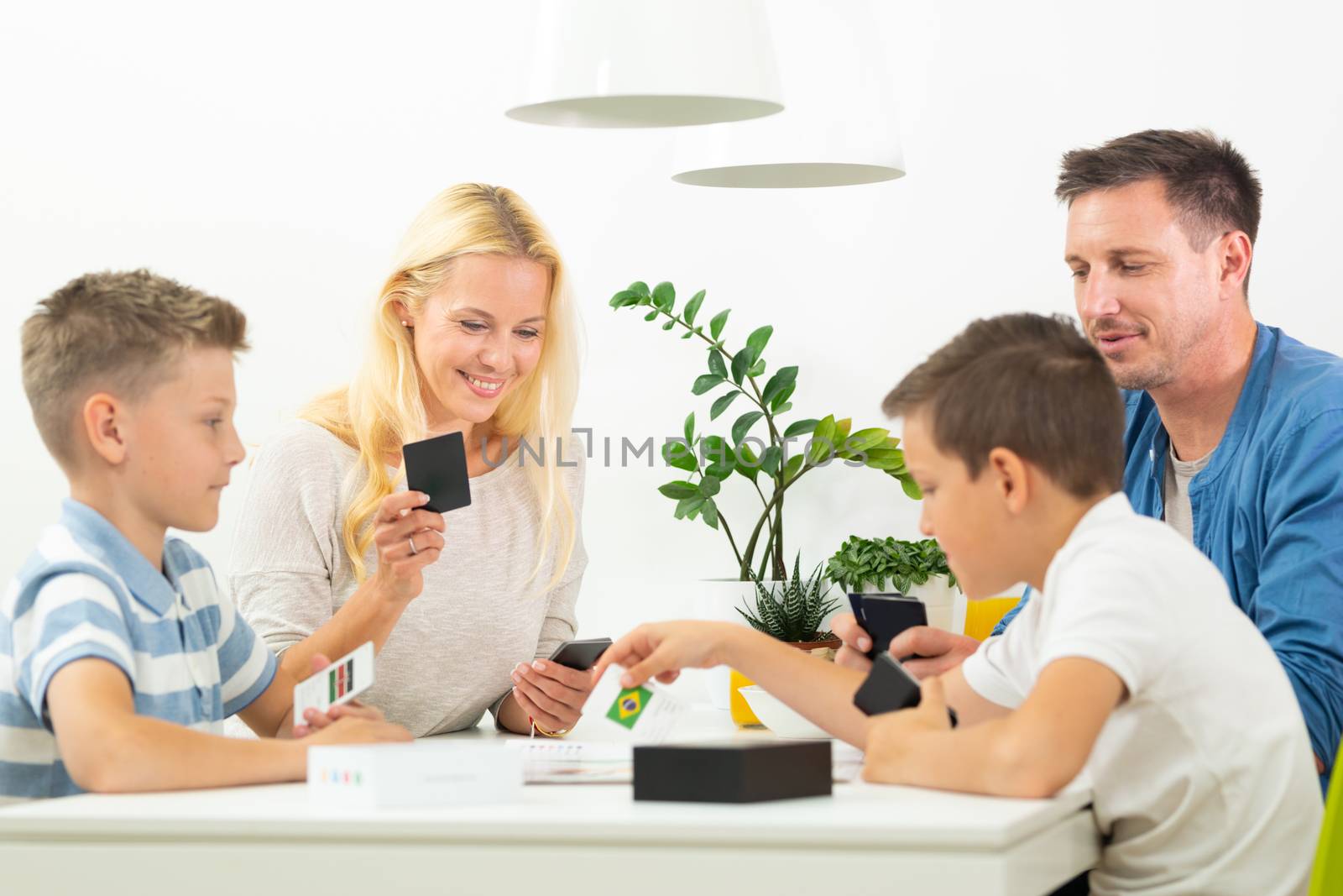 Happy young family playing card game at dining table at bright modern home. by kasto