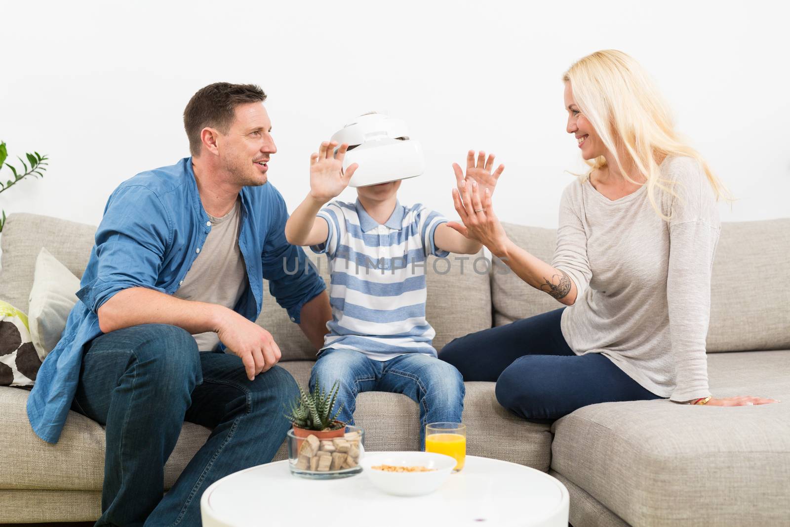 Happy caucasian family at home on living room sofa having fun playing games using virtual reality headset.