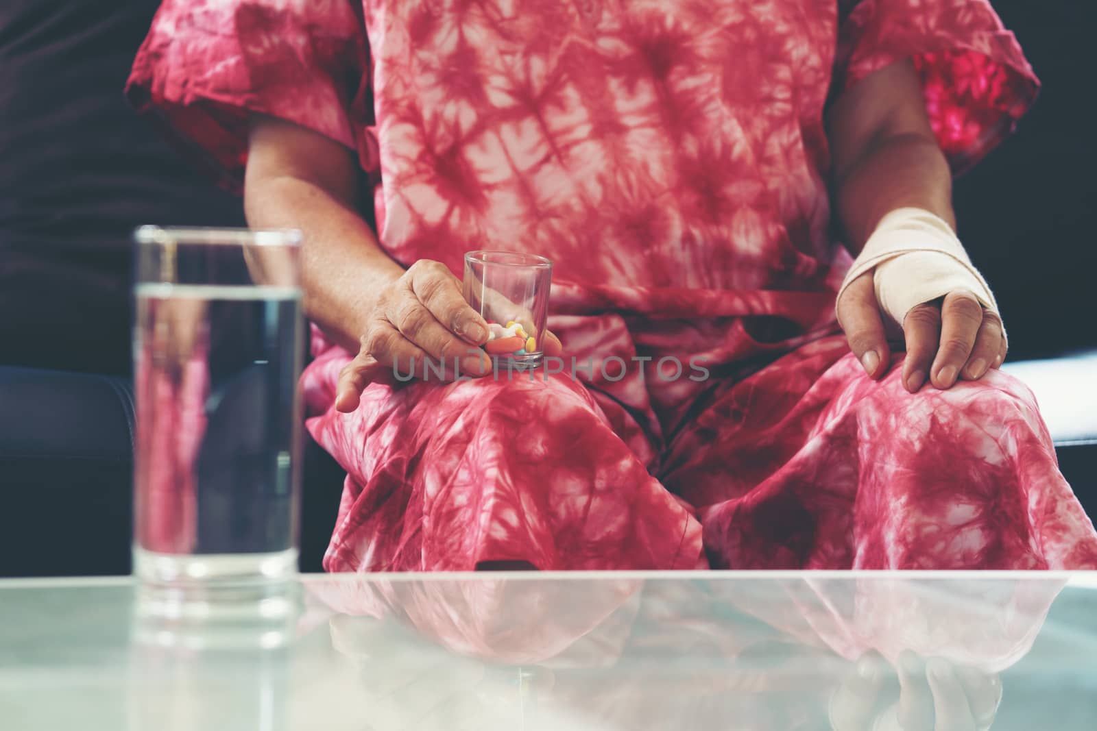 Senior asian woman take pill medicine on hand while sitting on sofa at home 