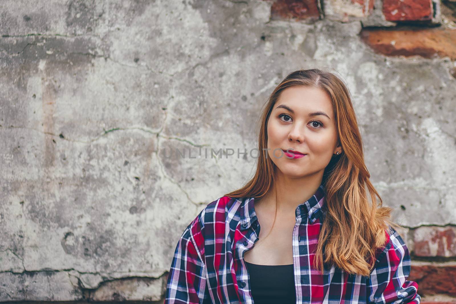 Beautiful girl is looking at camera and standing against brick wall