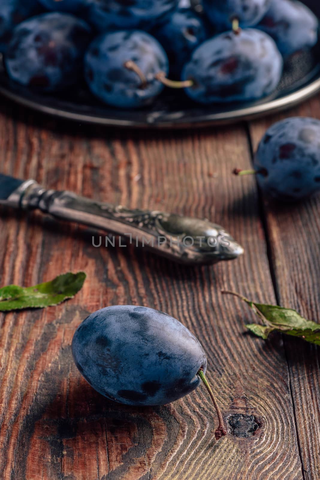 Ripe plums on metal tray and dark wooden surface with leaves and vintage knife