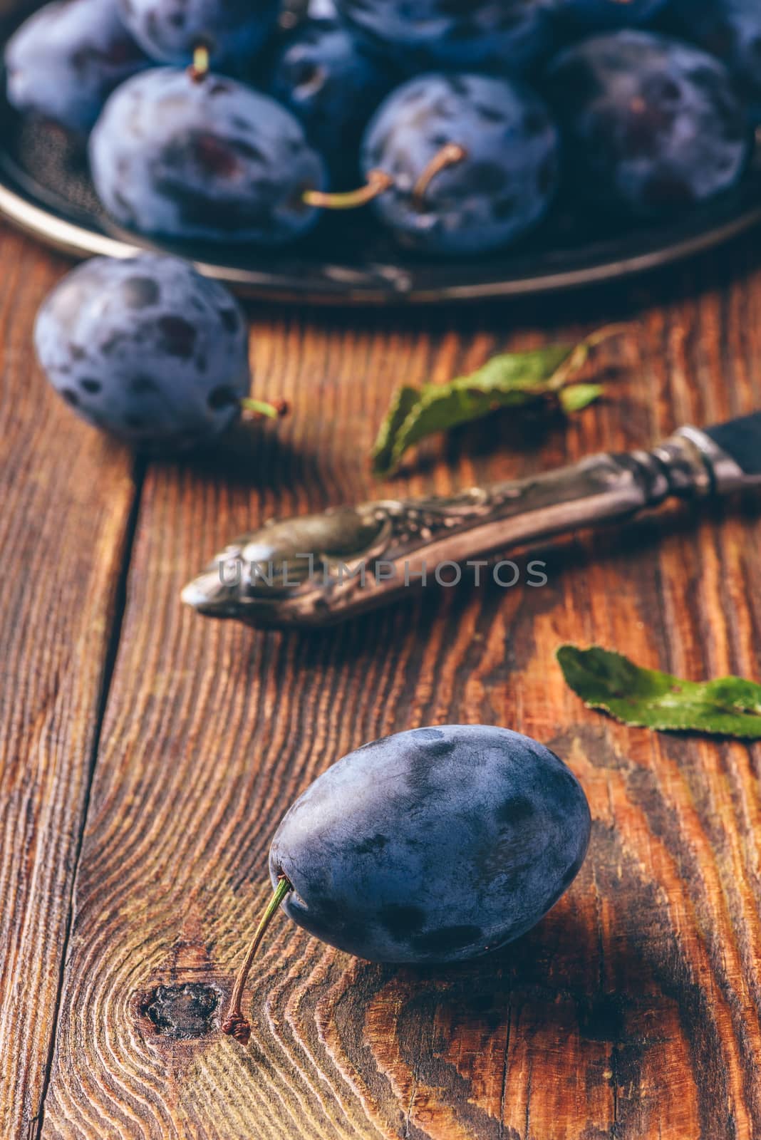 Ripe plums on metal tray and dark wooden surface with leaves and vintage knife