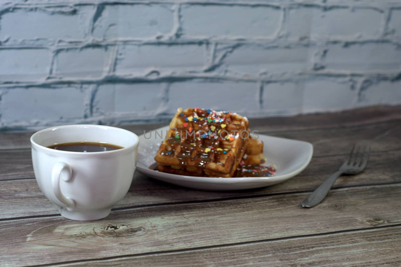 Tasty breakfast with a cup of coffee and two Viennese waffles with sprinkles and icing.