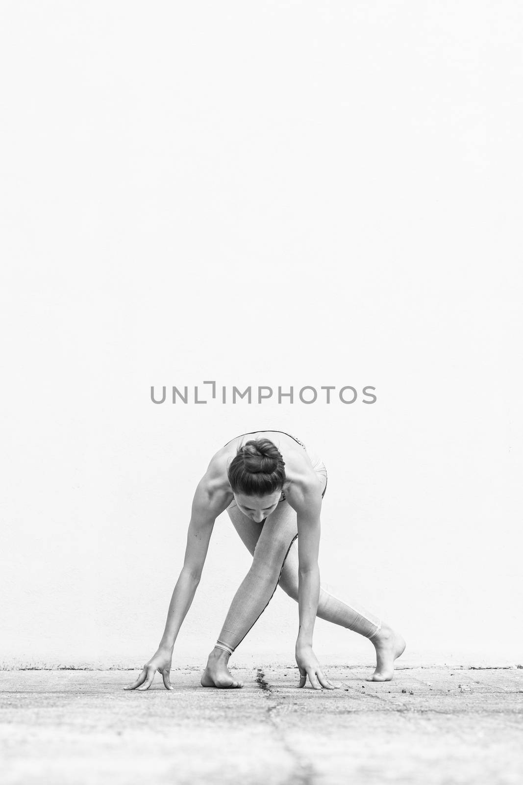 Fit sporty active girl in fashion sportswear doing yoga fitness exercise in front of gray wall, outdoor sports, urban style. Black and white image.