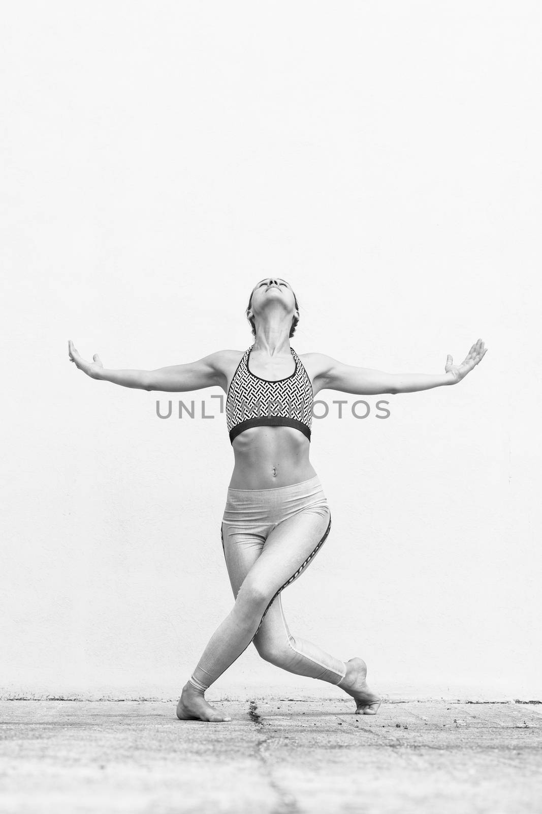 Fit sporty active girl in fashion sportswear doing yoga fitness exercise in front of gray wall, outdoor sports, urban style. Black and white image.