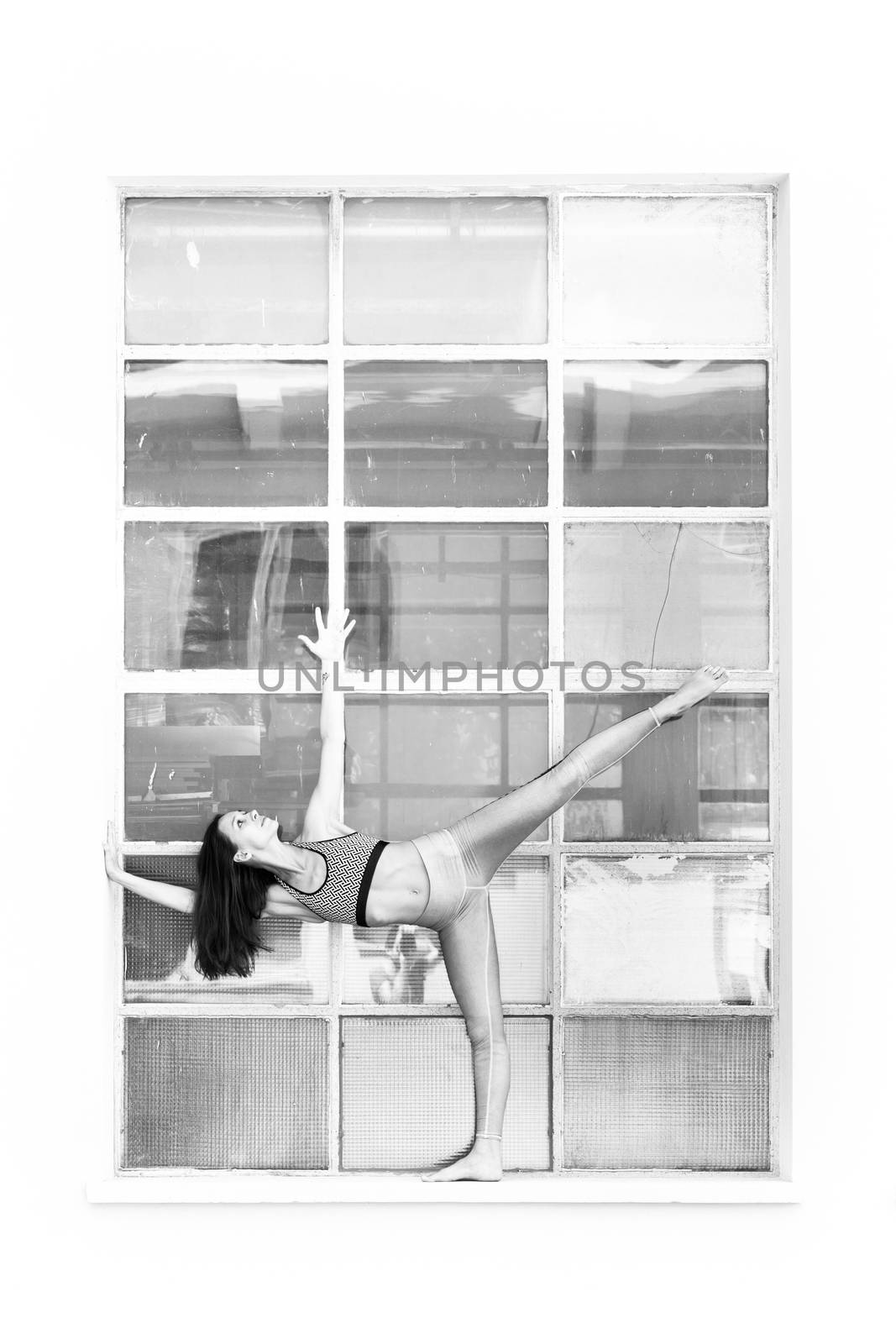Fit sporty active girl in fashion sportswear doing yoga fitness exercise in front of big industrial window frame. colorful reflections in window glass. Urban style yoga. Black and white.