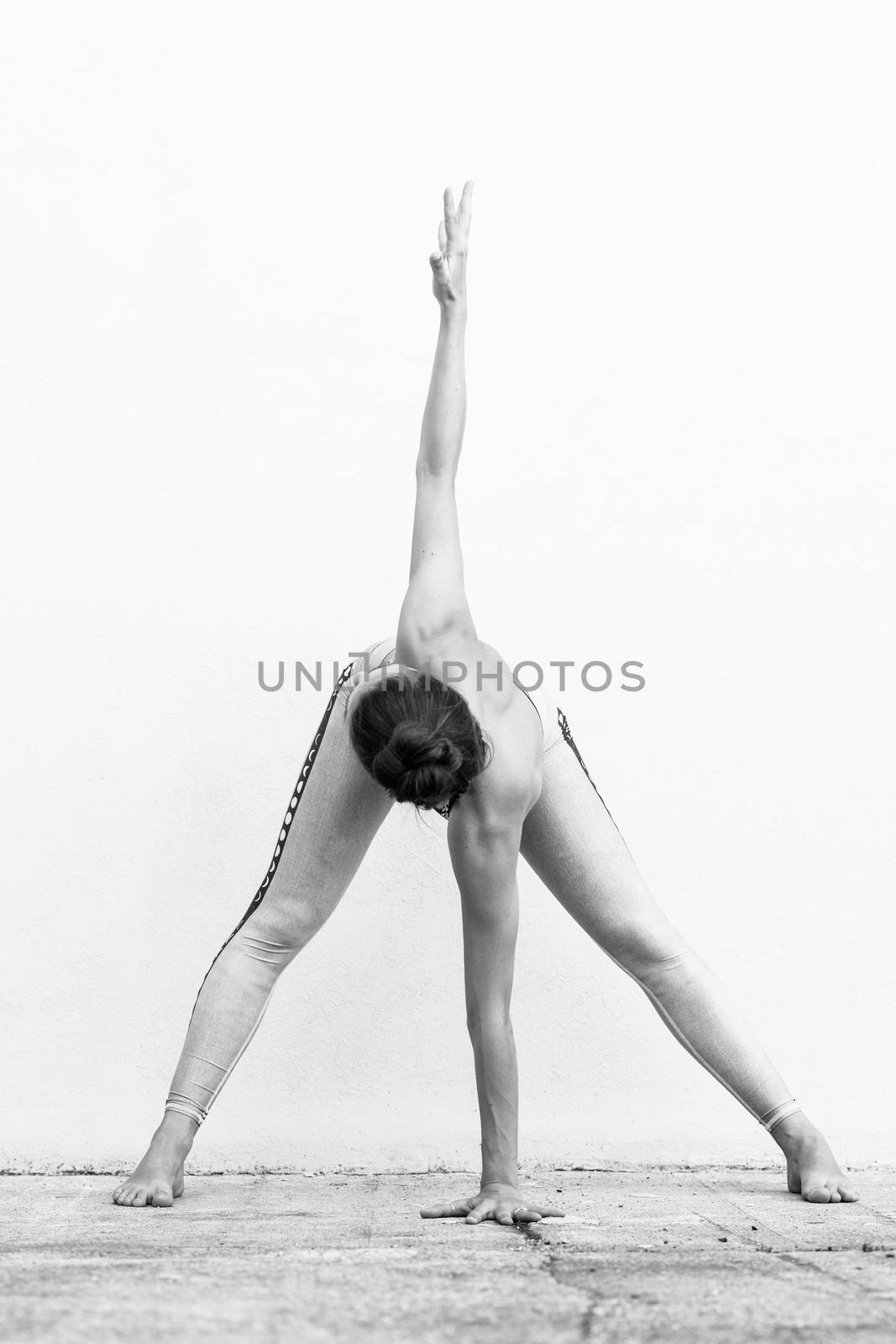 Fit sporty active girl in fashion sportswear doing yoga fitness exercise in front of gray wall, outdoor sports, urban style. Black and white photo. by kasto