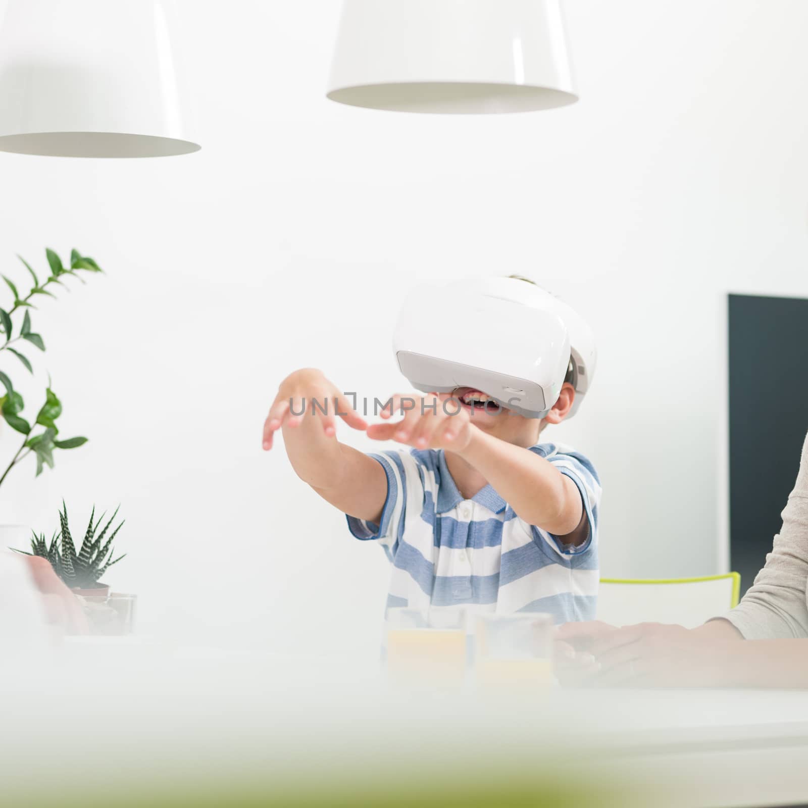 Amazed child using virtual reality headsets trying to grab unexisting virtual objects while sitting at the dinner table. by kasto