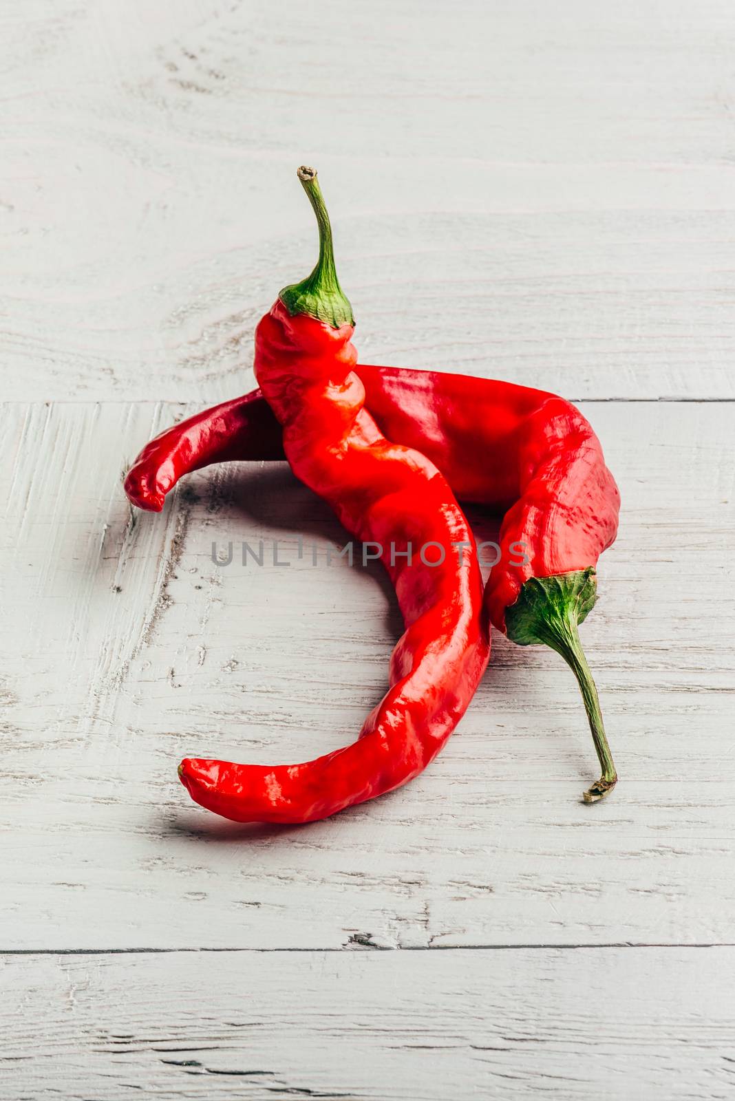 Ripe and red chili peppers over light wooden background.