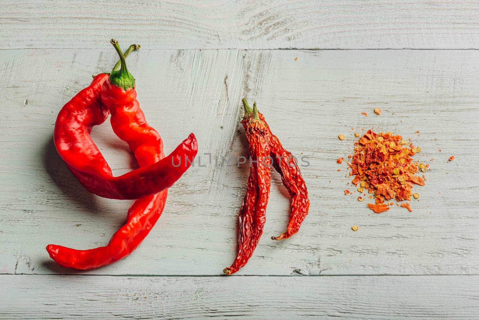 Fresh, dried and crushed red chili pepper over colored wooden background