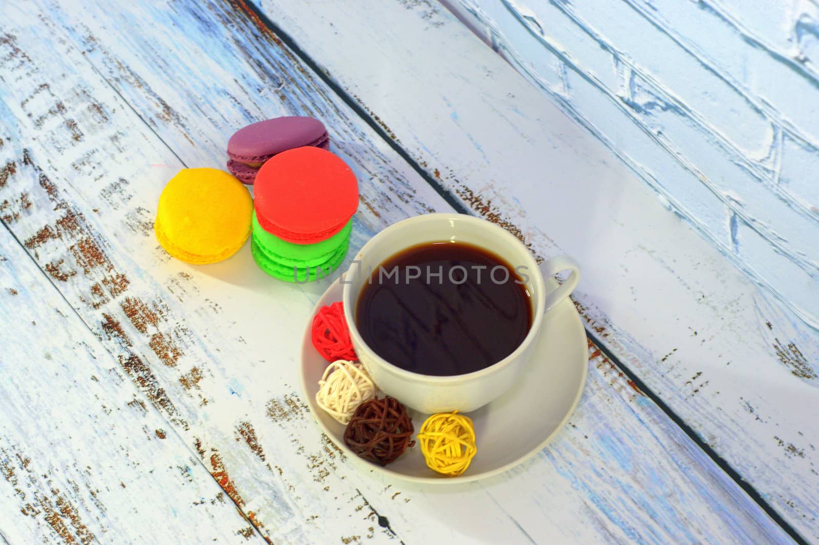 A cup of black coffee with balls for decor and four multi-colored macaroons.